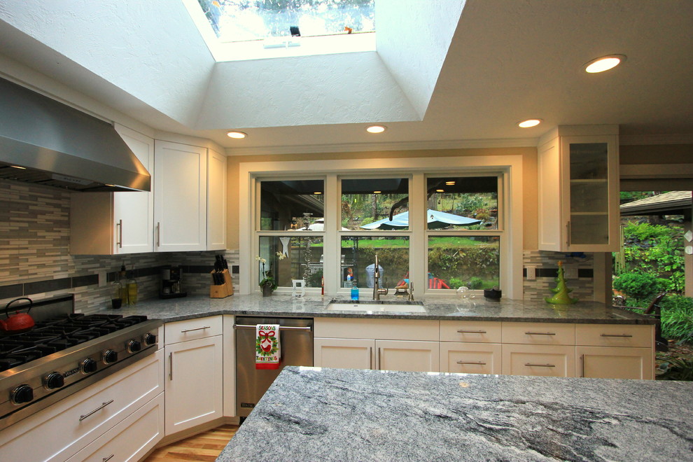 Large transitional u-shaped light wood floor open concept kitchen photo with an undermount sink, shaker cabinets, white cabinets, granite countertops, multicolored backsplash, mosaic tile backsplash, stainless steel appliances and an island