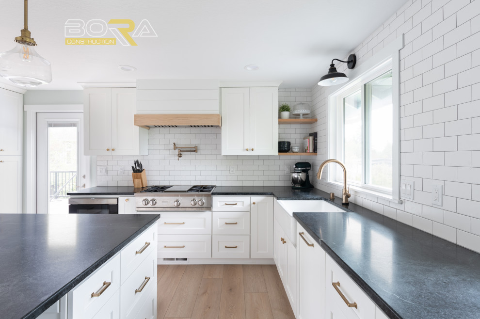 Mid-sized transitional u-shaped medium tone wood floor and brown floor eat-in kitchen photo in Seattle with shaker cabinets, white cabinets, quartz countertops, white backsplash, ceramic backsplash, stainless steel appliances, an island and black countertops