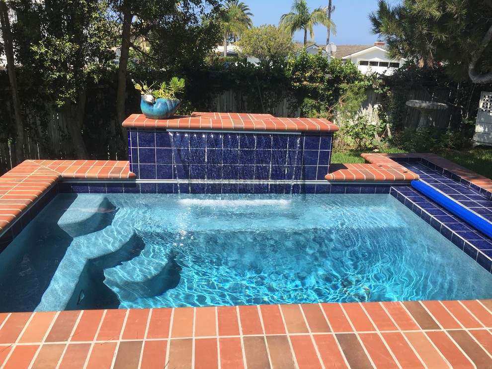 Photo of a small traditional backyard rectangular pool in Orange County with a water feature and brick pavers.