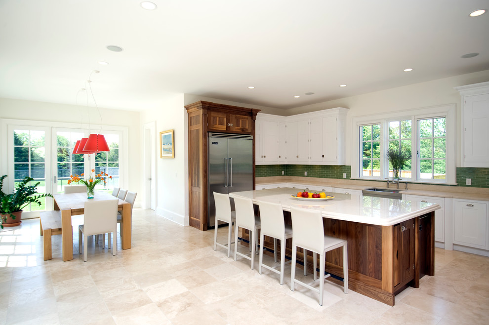 Contemporary u-shaped eat-in kitchen in New York with a farmhouse sink, shaker cabinets, white cabinets, marble benchtops, green splashback, glass tile splashback, stainless steel appliances and travertine floors.
