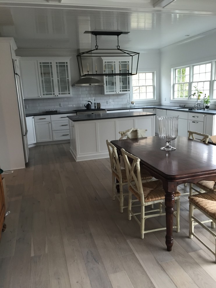 Large beach style u-shaped open plan kitchen in New York with a double-bowl sink, beaded inset cabinets, white cabinets, soapstone benchtops, white splashback, subway tile splashback, stainless steel appliances, light hardwood floors and with island.