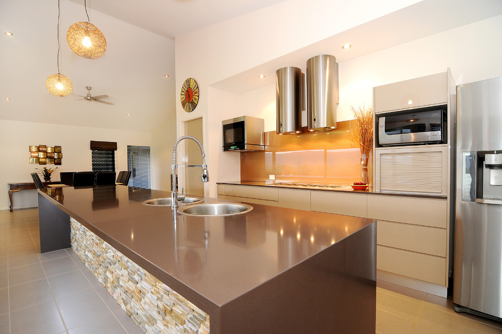 This is an example of a contemporary kitchen in Cairns with a drop-in sink, flat-panel cabinets, brown cabinets, granite benchtops, metallic splashback, glass sheet splashback, stainless steel appliances, ceramic floors and with island.