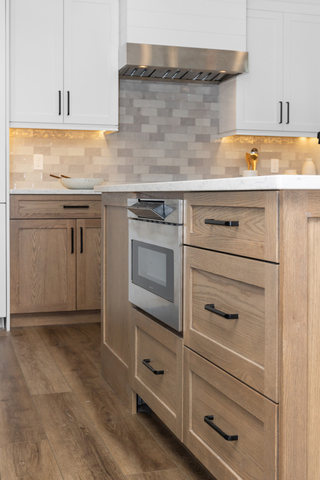 Mid-sized transitional eat-in kitchen photo with shaker cabinets, white cabinets, quartz countertops, gray backsplash, subway tile backsplash, stainless steel appliances, an island and white countertops