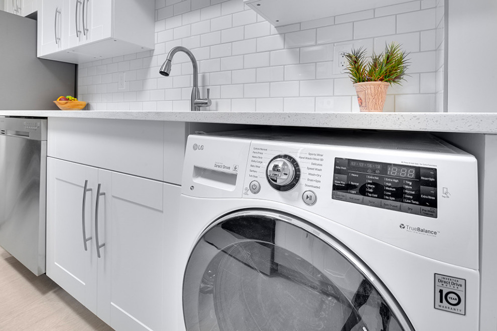 Mid-sized scandinavian galley laundry room in Vancouver with a double-bowl sink, flat-panel cabinets, white cabinets, quartzite benchtops, white splashback, ceramic splashback, vinyl floors, grey floor and white benchtop.
