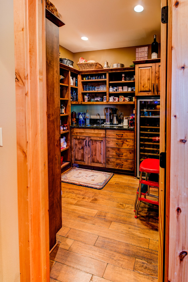 This is an example of a mid-sized country l-shaped kitchen pantry in Minneapolis with medium hardwood floors, brown floor, an undermount sink, raised-panel cabinets, medium wood cabinets, granite benchtops, grey splashback, slate splashback, stainless steel appliances and with island.