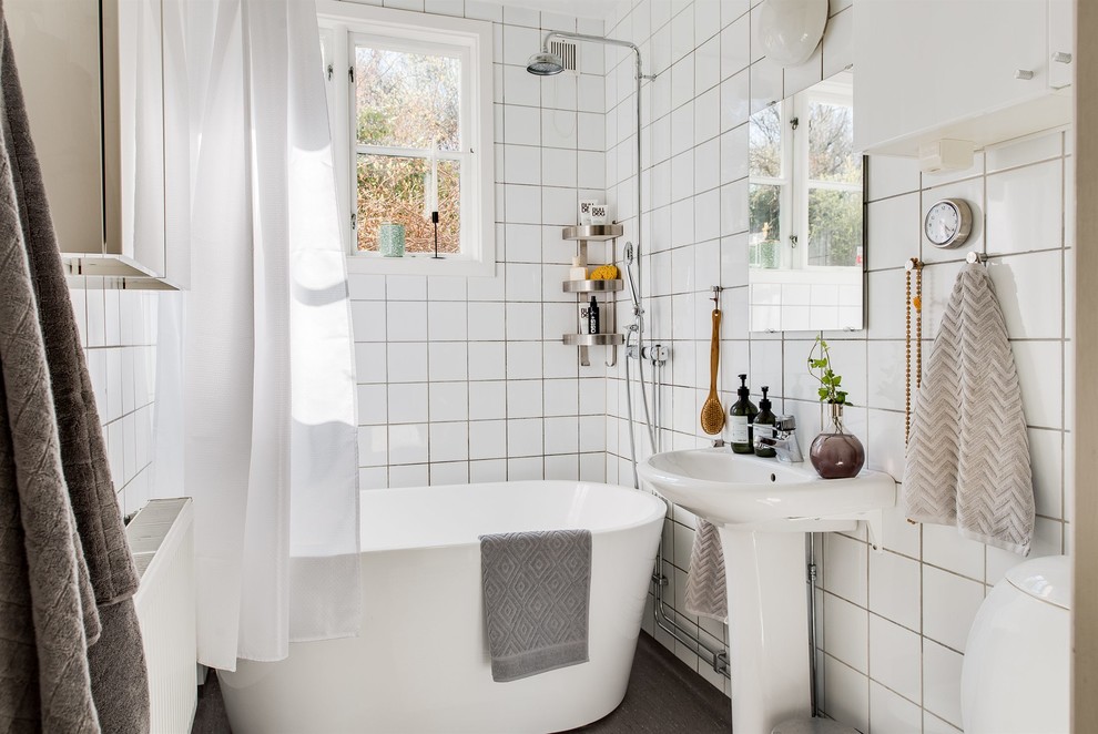 Photo of a small scandinavian bathroom in Gothenburg with a freestanding tub, a shower/bathtub combo, porcelain tile, white walls, a console sink and black floor.
