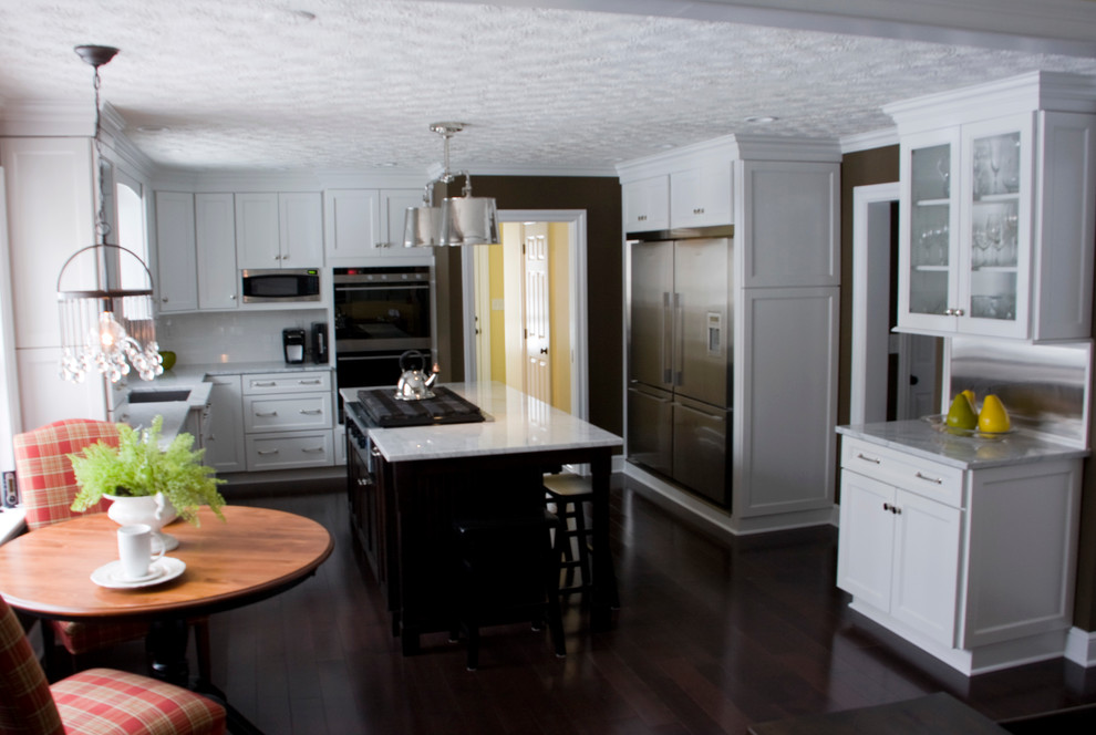 Large transitional dark wood floor kitchen photo with an undermount sink, white cabinets, marble countertops, white backsplash, glass tile backsplash, stainless steel appliances and an island