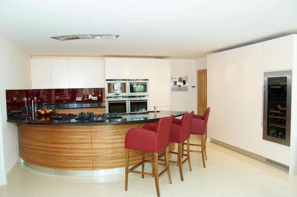 Mid-sized contemporary u-shaped eat-in kitchen in Oxfordshire with a double-bowl sink, flat-panel cabinets, medium wood cabinets, granite benchtops, red splashback, glass sheet splashback, stainless steel appliances, porcelain floors and with island.