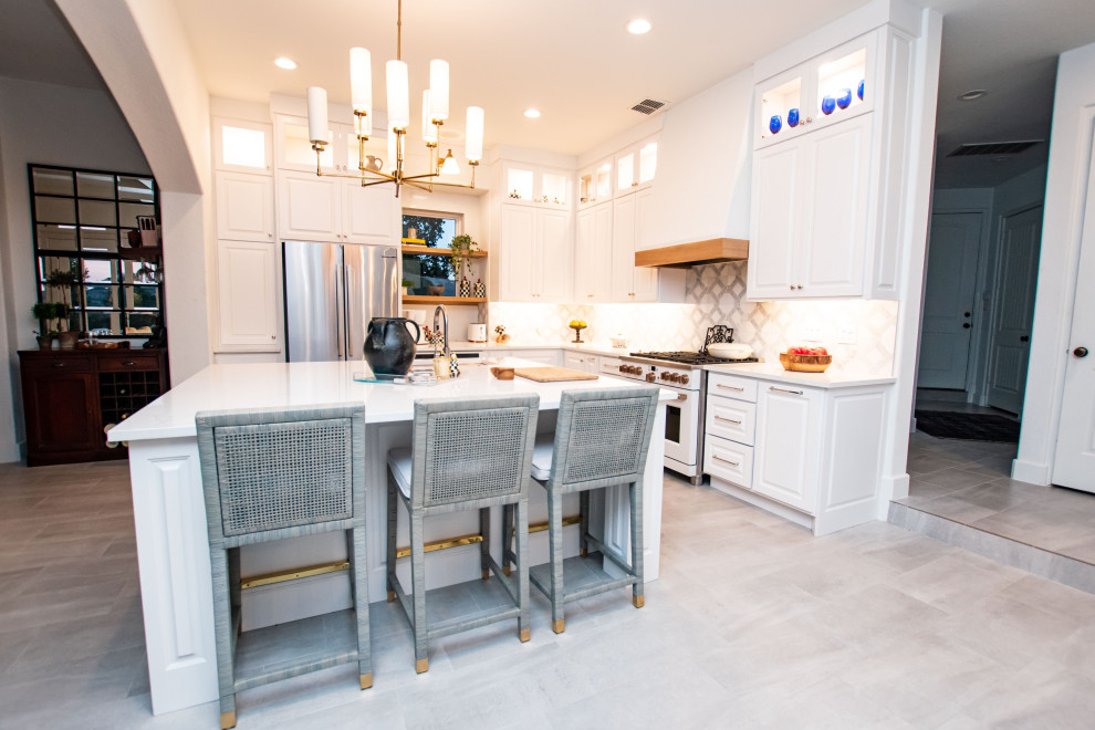 Inspiration for a transitional l-shaped porcelain tile and gray floor eat-in kitchen remodel in Austin with an undermount sink, raised-panel cabinets, white cabinets, quartz countertops, white backsplash, marble backsplash, white appliances, an island and white countertops