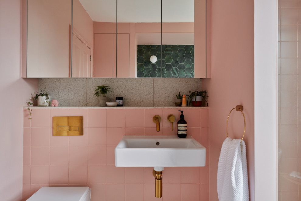 Foto på ett mellanstort funkis flerfärgad badrum för barn, med ett fristående badkar, en kantlös dusch, en vägghängd toalettstol, rosa kakel, keramikplattor, rosa väggar, cementgolv, ett väggmonterat handfat, bänkskiva i terrazo, rosa golv och dusch med skjutdörr