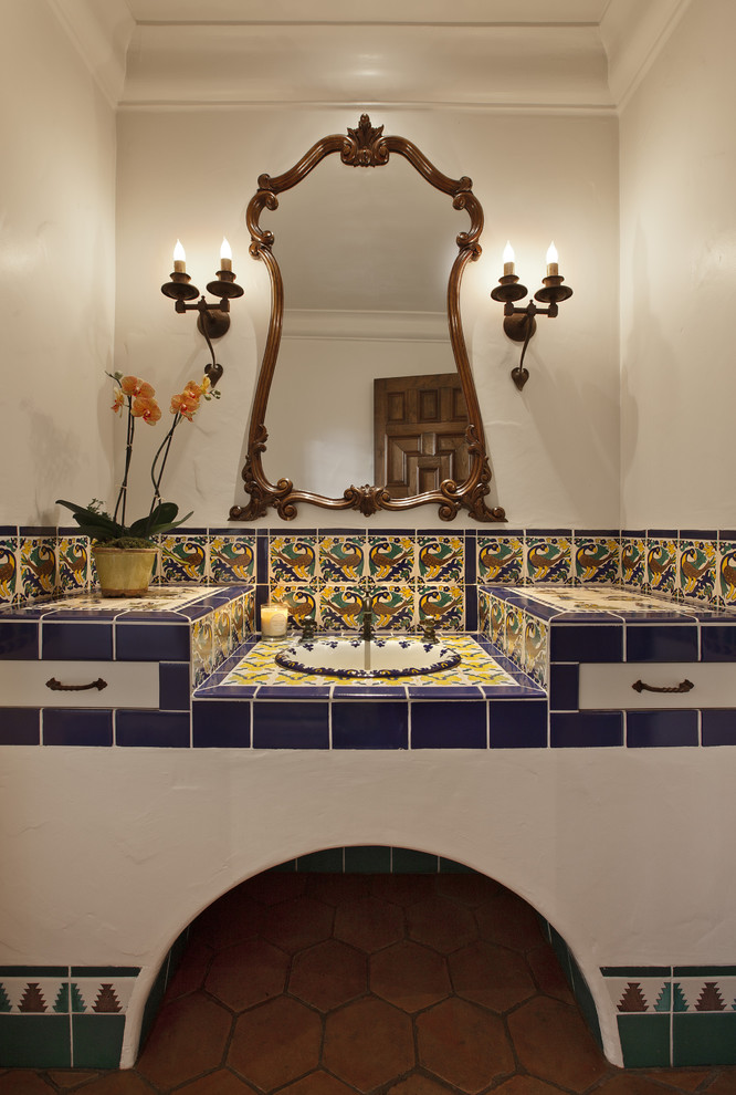 This is an example of a mediterranean bathroom in Santa Barbara with a drop-in sink, multi-coloured tile, ceramic tile, tile benchtops, white walls and terra-cotta floors.