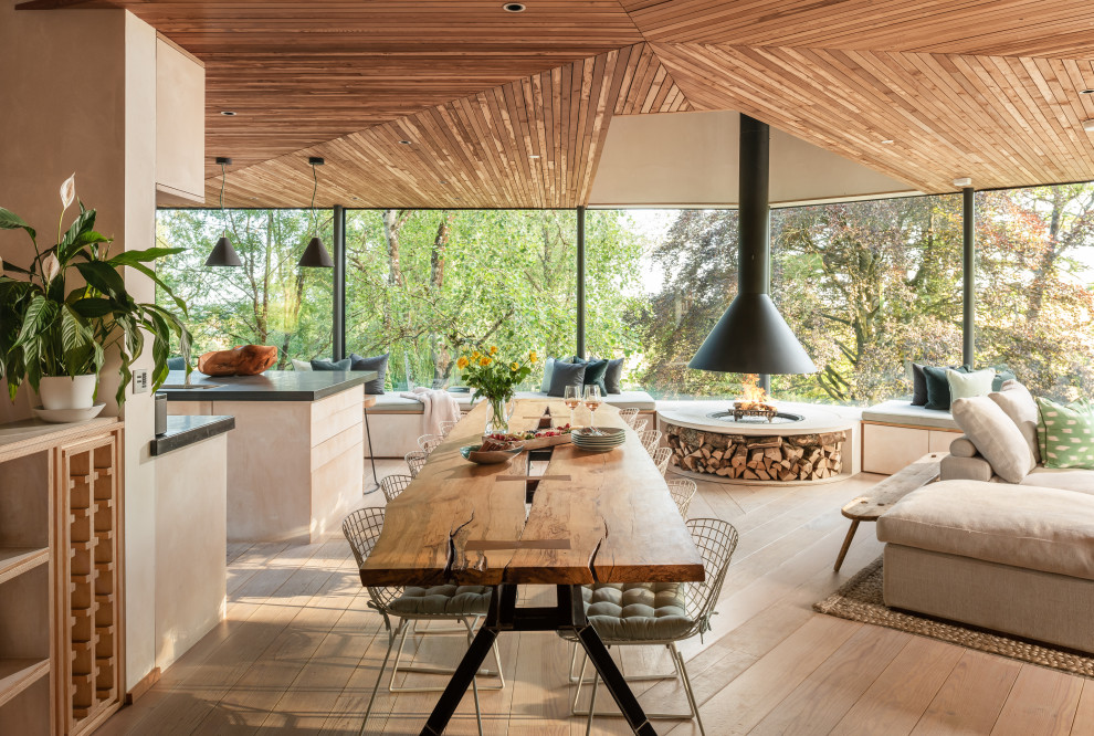 Photo of an expansive country open plan dining in Devon with medium hardwood floors, a hanging fireplace, a concrete fireplace surround and wood.
