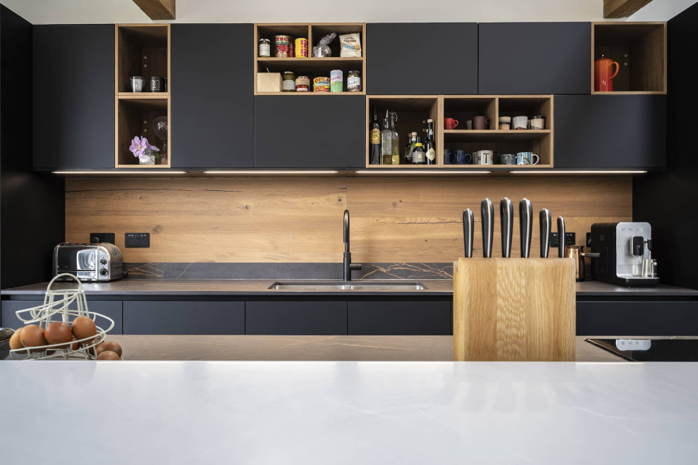 Design ideas for a mid-sized modern single-wall open plan kitchen in Oxfordshire with a double-bowl sink, flat-panel cabinets, black cabinets, quartzite benchtops, brown splashback, timber splashback, black appliances, with island, black floor, multi-coloured benchtop and exposed beam.