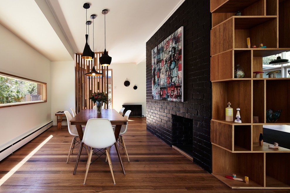 Inspiration for a mid-sized contemporary dining room in Melbourne with black walls, medium hardwood floors, a standard fireplace and a brick fireplace surround.