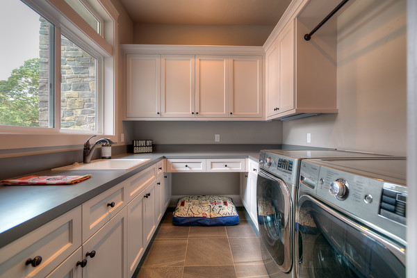 Design ideas for a large country galley dedicated laundry room in Portland with a drop-in sink, shaker cabinets, white cabinets, quartz benchtops, beige walls, a side-by-side washer and dryer, grey floor, porcelain floors and grey benchtop.