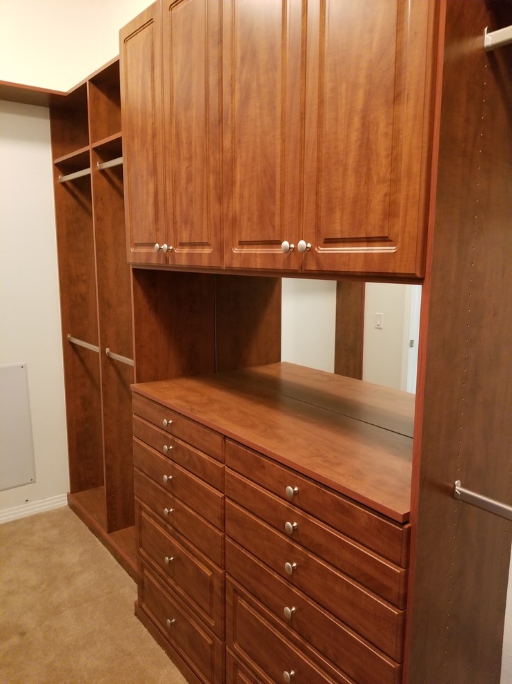 Inspiration for a small traditional gender-neutral walk-in wardrobe in Los Angeles with raised-panel cabinets, medium wood cabinets, carpet and brown floor.