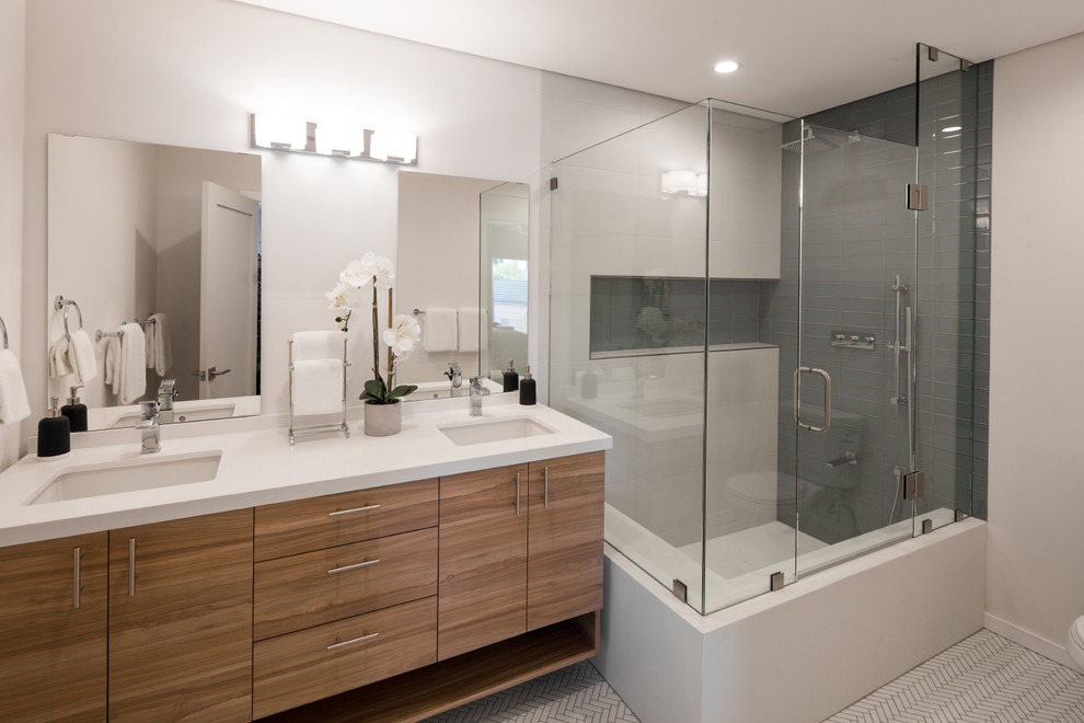 This is an example of a large contemporary 3/4 bathroom in Los Angeles with flat-panel cabinets, medium wood cabinets, a corner shower, gray tile, porcelain tile, white walls, porcelain floors, an undermount sink, engineered quartz benchtops, white floor and a hinged shower door.