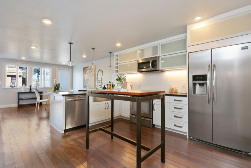Design ideas for an expansive modern l-shaped eat-in kitchen in San Francisco with a farmhouse sink, glass-front cabinets, white cabinets, granite benchtops, white splashback, subway tile splashback, stainless steel appliances, dark hardwood floors and a peninsula.