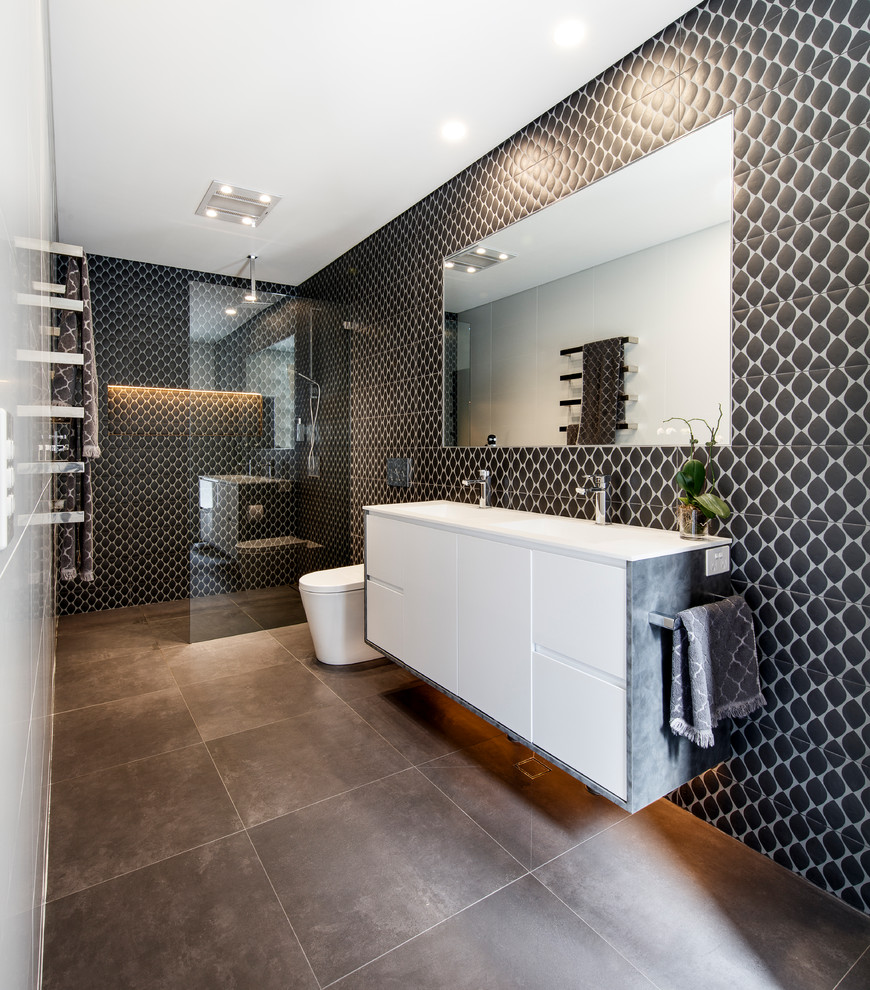 Expansive contemporary 3/4 bathroom in Sydney with flat-panel cabinets, white cabinets, a curbless shower, a one-piece toilet, black tile, an integrated sink, brown floor, an open shower, white benchtops, porcelain tile, brown walls, porcelain floors and solid surface benchtops.