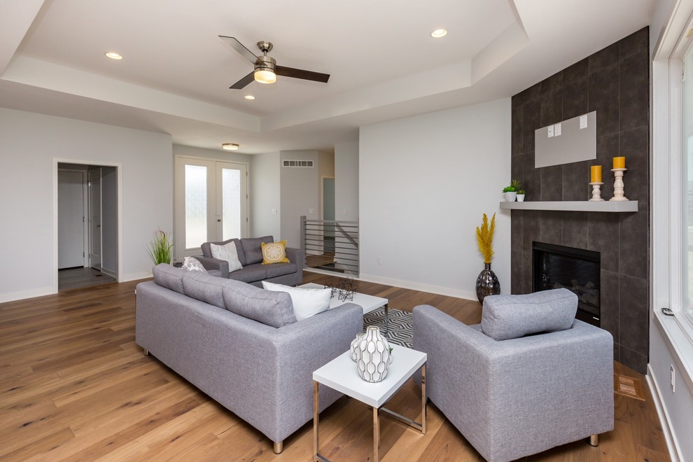This is an example of a modern open concept living room in Other with grey walls, medium hardwood floors, a corner fireplace, a tile fireplace surround, a wall-mounted tv and multi-coloured floor.