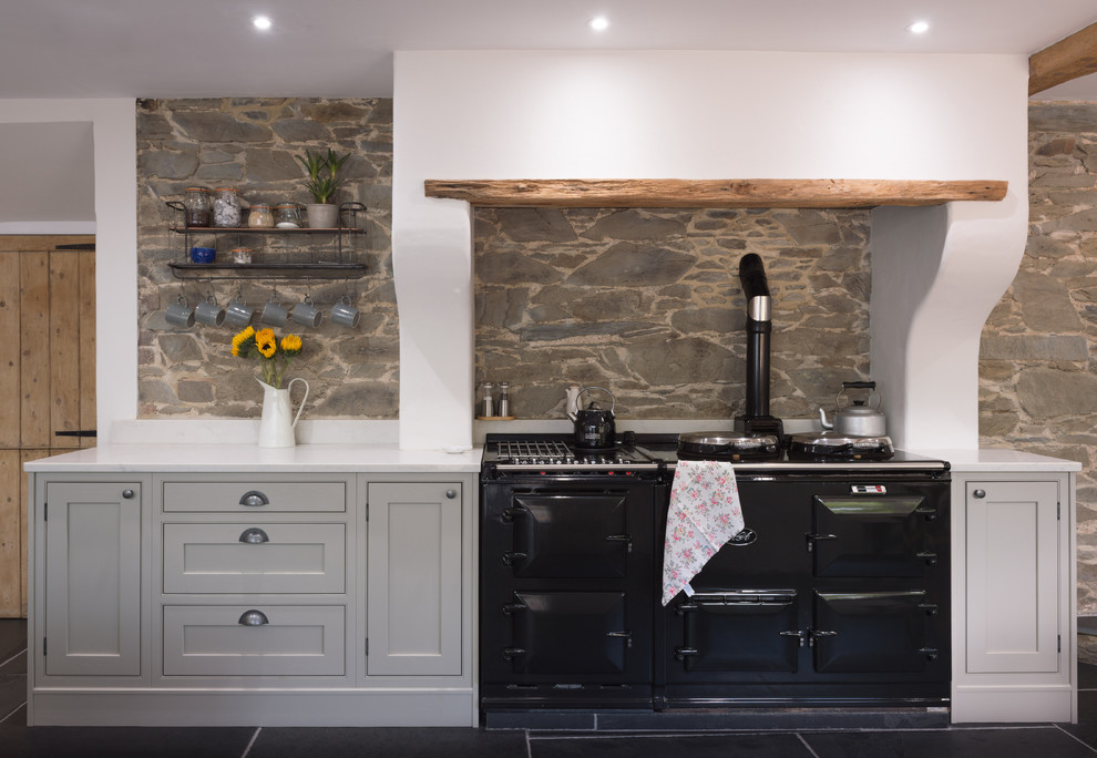 Large l-shaped eat-in kitchen in Cornwall with a farmhouse sink, shaker cabinets, grey cabinets, granite benchtops, white splashback, cement tile splashback, black appliances, slate floors, with island, grey floor and white benchtop.
