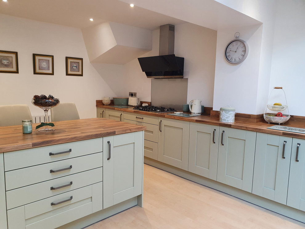 Inspiration for a mid-sized contemporary single-wall open plan kitchen in West Midlands with shaker cabinets, green cabinets, laminate benchtops, grey splashback, glass tile splashback, with island and brown benchtop.