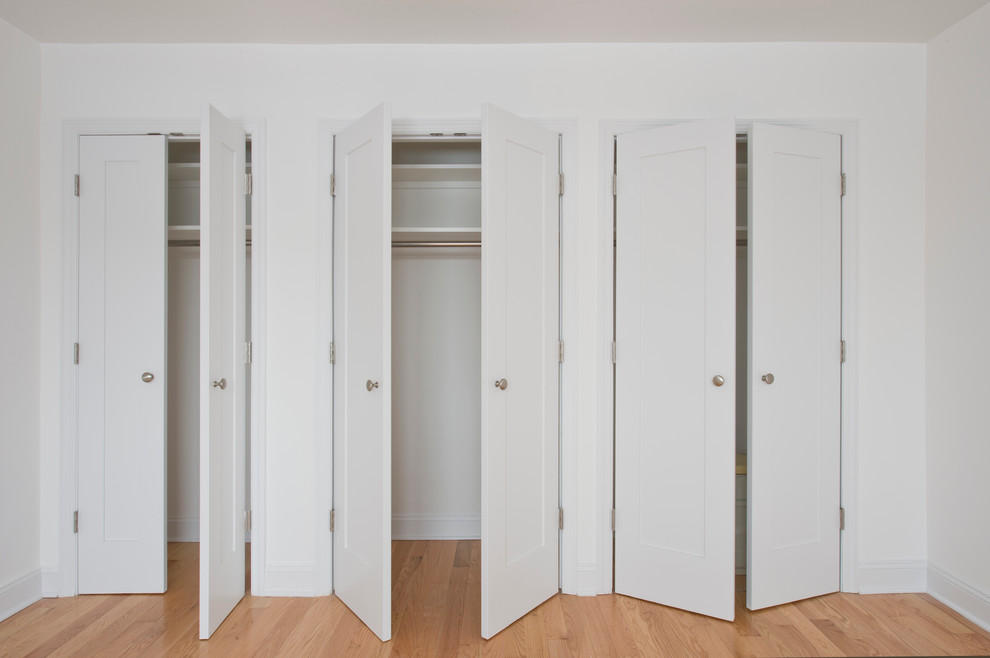 This is an example of a large contemporary gender-neutral built-in wardrobe in New York with shaker cabinets, white cabinets and light hardwood floors.