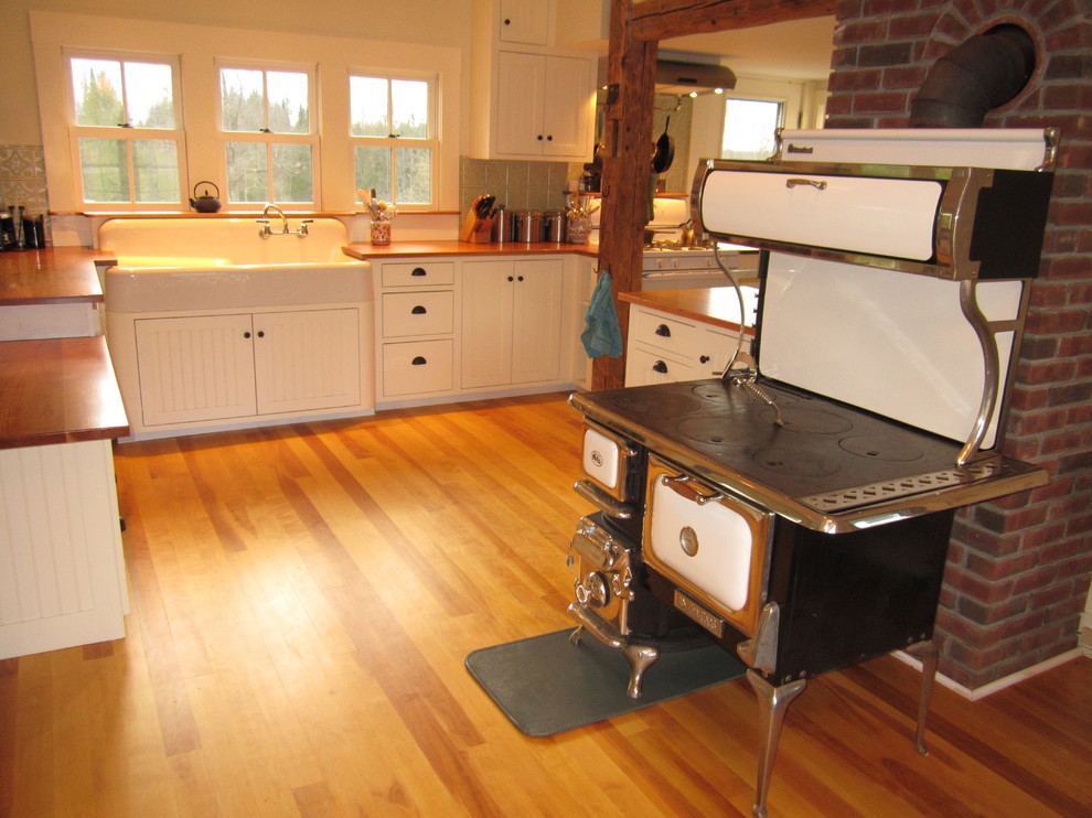 Country kitchen in Burlington with a farmhouse sink, white cabinets, wood benchtops and beaded inset cabinets.