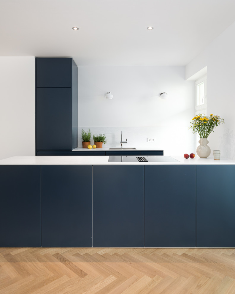 This is an example of a contemporary u-shaped kitchen in Berlin with an undermount sink, flat-panel cabinets, blue cabinets, light hardwood floors, a peninsula, beige floor and white benchtop.