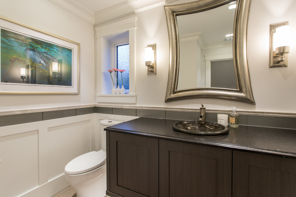 Inspiration for a mid-sized transitional bathroom in Vancouver with shaker cabinets, brown cabinets, a one-piece toilet, gray tile, glass tile, grey walls, medium hardwood floors, a vessel sink, granite benchtops, beige floor and black benchtops.