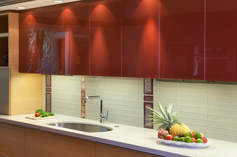 Photo of a tropical kitchen in Hawaii with a single-bowl sink, flat-panel cabinets, medium wood cabinets, quartzite benchtops, red splashback, glass tile splashback, panelled appliances, porcelain floors and multiple islands.
