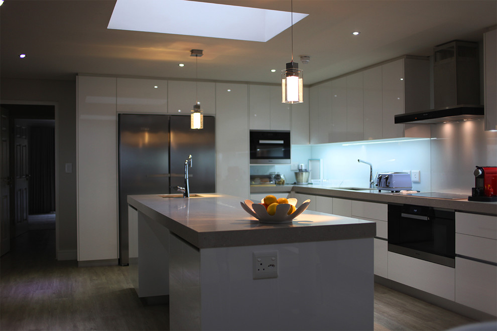 Design ideas for an expansive modern l-shaped eat-in kitchen in Other with an undermount sink, glass-front cabinets, white cabinets, quartz benchtops, white splashback, glass sheet splashback and with island.