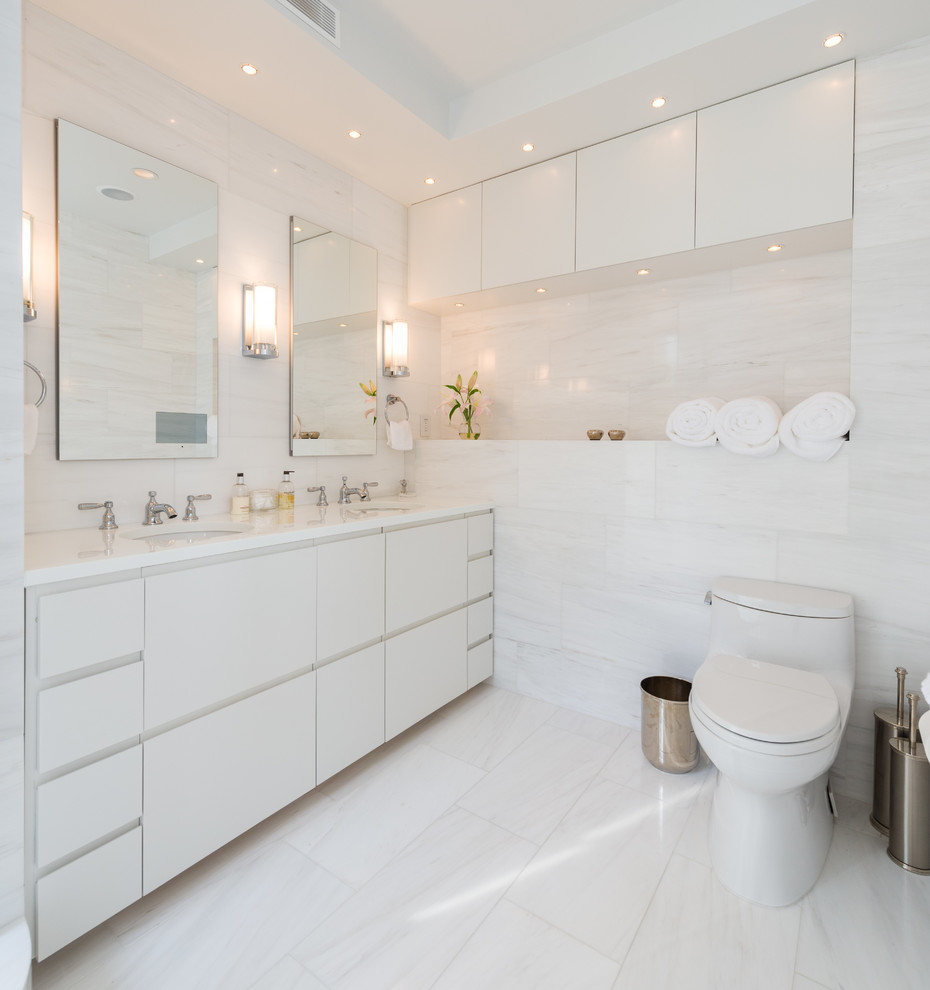 Photo of a contemporary bathroom in New York with flat-panel cabinets, white cabinets, quartzite benchtops, a one-piece toilet, white tile, stone tile, an undermount sink and white benchtops.