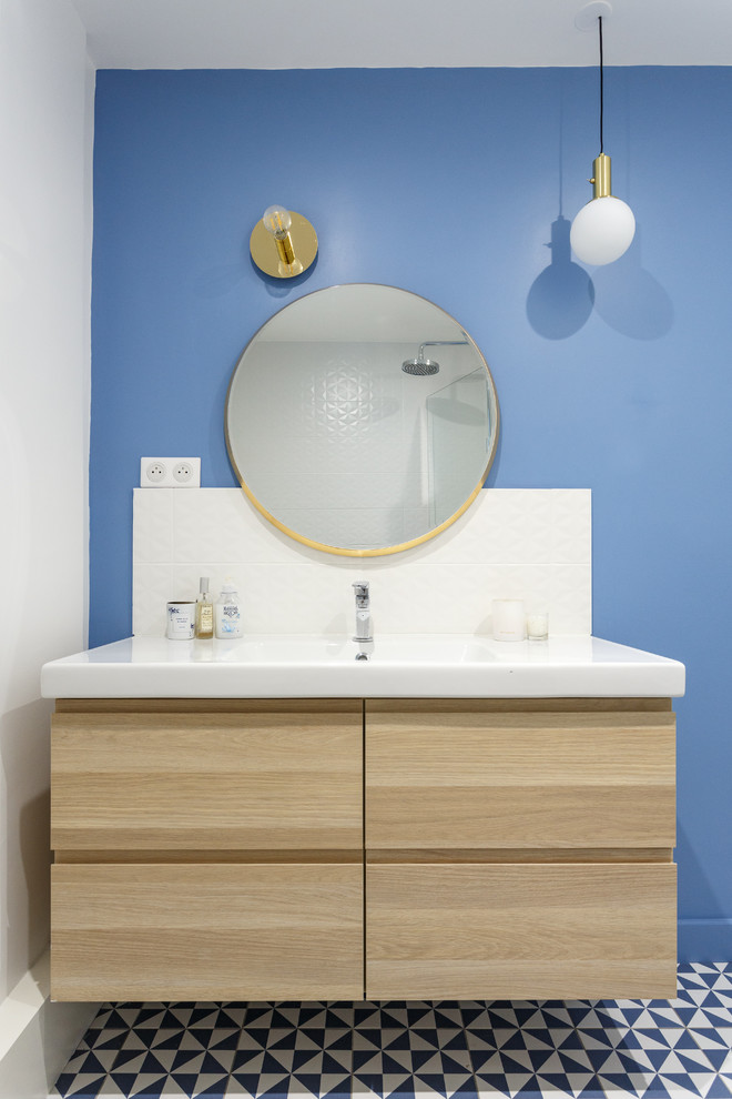 Small modern master bathroom in Paris with flat-panel cabinets, medium wood cabinets, an alcove tub, a shower/bathtub combo, a two-piece toilet, white tile, ceramic tile, blue walls, cement tiles, a trough sink, solid surface benchtops, blue floor and white benchtops.