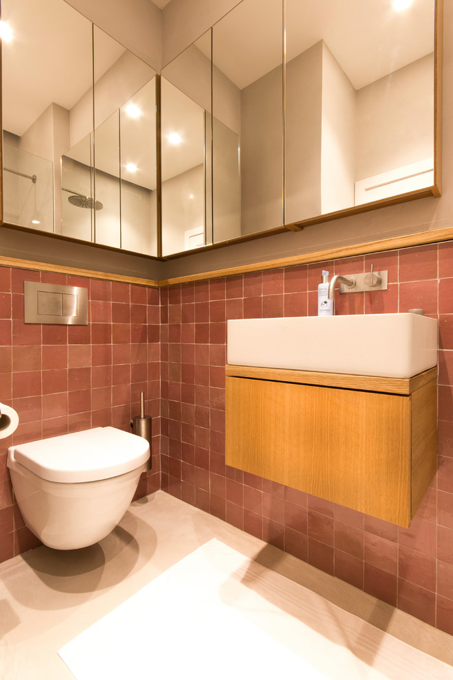 This is an example of a large traditional 3/4 bathroom in London with furniture-like cabinets, brown cabinets, an open shower, a wall-mount toilet, brown tile, terra-cotta tile, beige walls, a wall-mount sink, wood benchtops, beige floor and an open shower.
