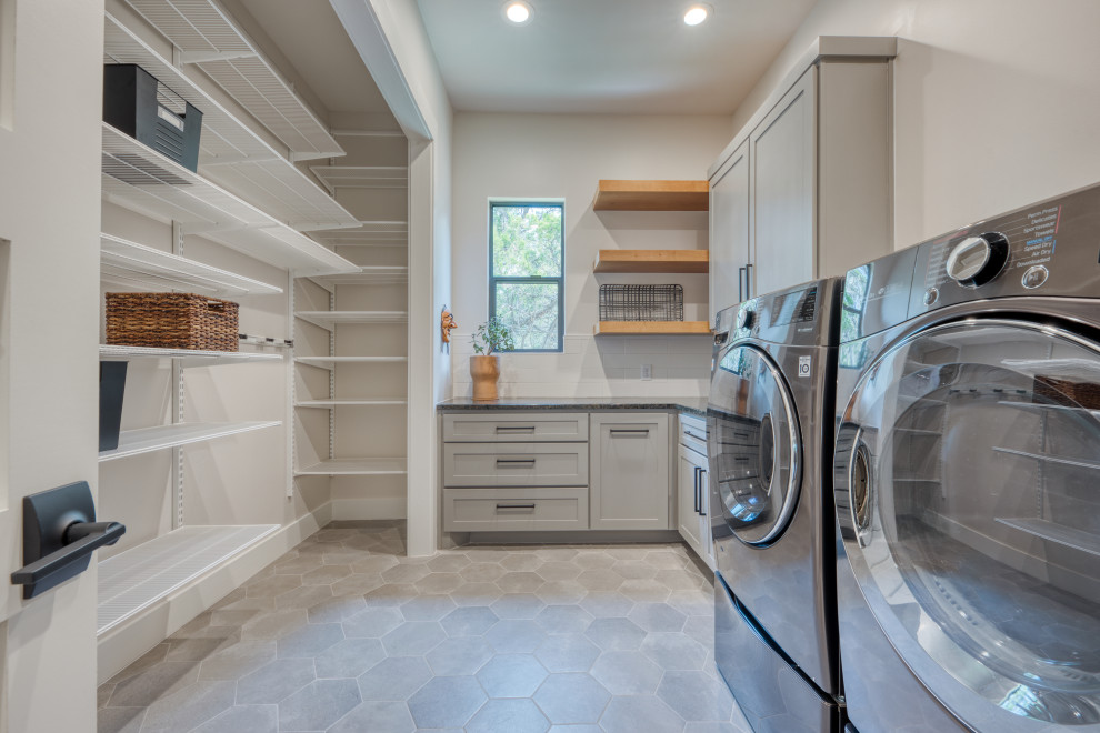 Photo of a mid-sized modern l-shaped dedicated laundry room in Austin with shaker cabinets, grey cabinets, soapstone benchtops, beige walls, concrete floors, a side-by-side washer and dryer, grey floor and black benchtop.