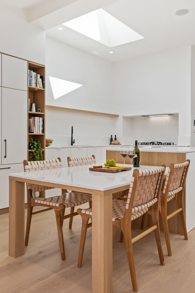 Design ideas for a mid-sized scandinavian l-shaped eat-in kitchen in Perth with an undermount sink, flat-panel cabinets, white cabinets, quartz benchtops, white splashback, mosaic tile splashback, black appliances, medium hardwood floors, with island, brown floor and white benchtop.