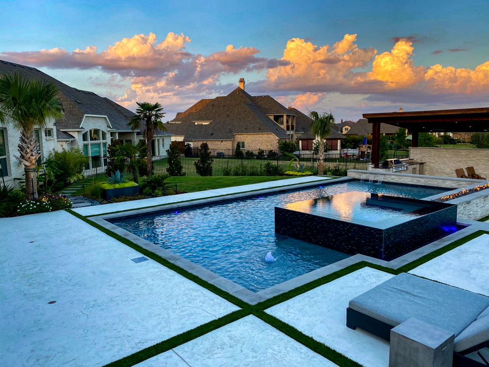 Design ideas for a large modern backyard custom-shaped infinity pool in Dallas with a water feature and stamped concrete.