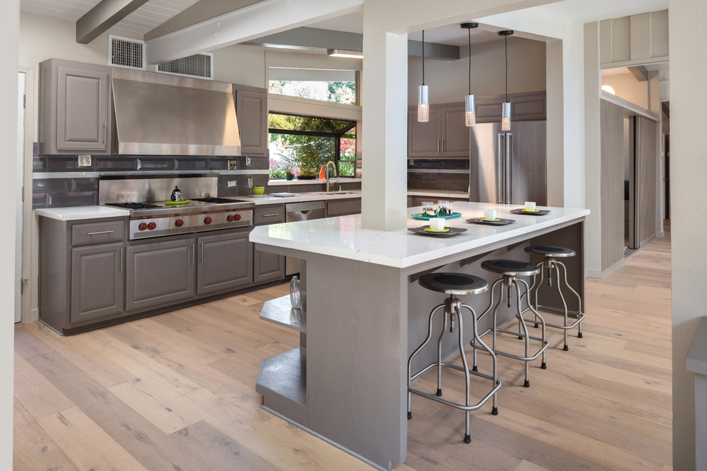 Inspiration for a large transitional l-shaped light wood floor and white floor eat-in kitchen remodel with an undermount sink, shaker cabinets, gray cabinets, solid surface countertops, multicolored backsplash, porcelain backsplash, stainless steel appliances, an island and white countertops