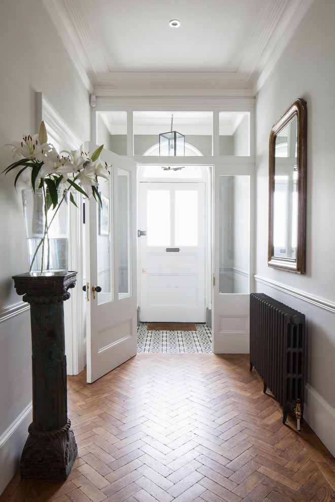 Photo of a large transitional foyer in Sussex with grey walls, light hardwood floors, a single front door, a white front door, brown floor, coffered and panelled walls.