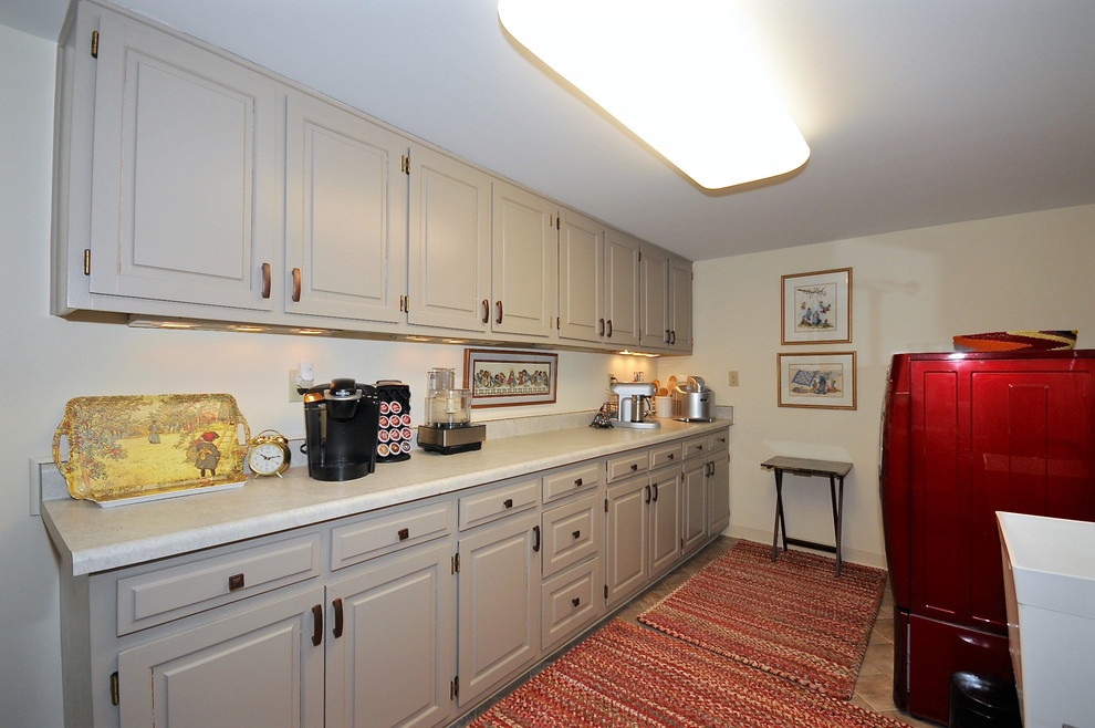 Mid-sized arts and crafts galley utility room in Indianapolis with an utility sink, raised-panel cabinets, white cabinets, solid surface benchtops, beige walls, ceramic floors and a side-by-side washer and dryer.