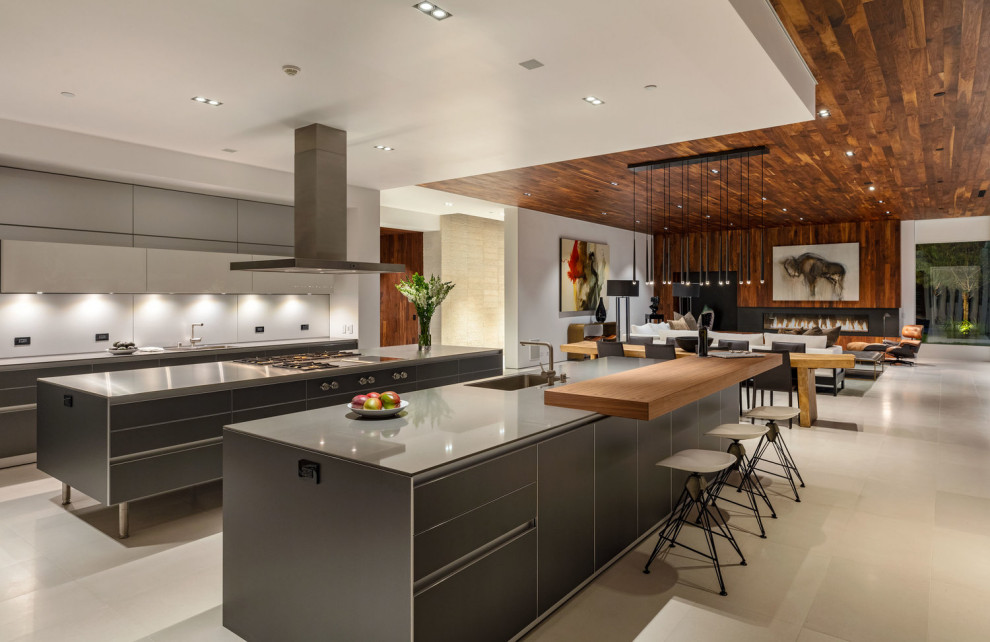 This is an example of an expansive contemporary kitchen/diner in Los Angeles with an integrated sink, flat-panel cabinets, black cabinets, marble worktops, grey splashback, stone tiled splashback, stainless steel appliances, multiple islands, beige floors and grey worktops.