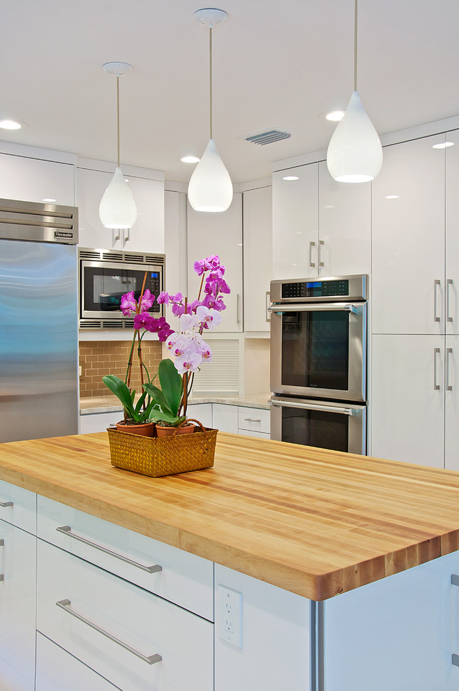 Inspiration for a large contemporary u-shaped eat-in kitchen in Jacksonville with an undermount sink, flat-panel cabinets, white cabinets, wood benchtops, beige splashback, subway tile splashback, stainless steel appliances, ceramic floors and with island.