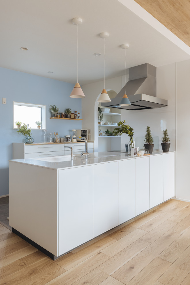 This is an example of a mid-sized scandinavian single-wall open plan kitchen in Other with flat-panel cabinets, white cabinets, white splashback, light hardwood floors, beige floor, white benchtop and wallpaper.