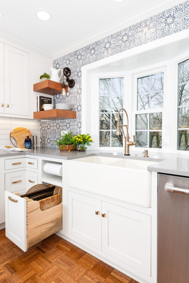Small eclectic l-shaped medium tone wood floor and brown floor kitchen pantry photo with a farmhouse sink, beaded inset cabinets, white cabinets, quartz countertops, blue backsplash, terra-cotta backsplash, stainless steel appliances, a peninsula and gray countertops