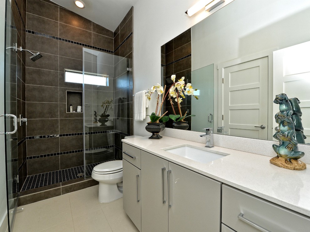 This is an example of a mid-sized contemporary 3/4 bathroom in Austin with flat-panel cabinets, grey cabinets, a curbless shower, brown tile, porcelain tile, white walls, porcelain floors, an undermount sink, engineered quartz benchtops, beige floor and a hinged shower door.
