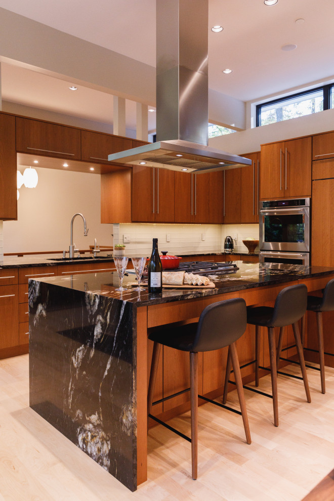 This is an example of a large contemporary u-shaped kitchen in Baltimore with an undermount sink, flat-panel cabinets, medium wood cabinets, beige splashback, glass tile splashback, stainless steel appliances, light hardwood floors, a peninsula, beige floor and black benchtop.
