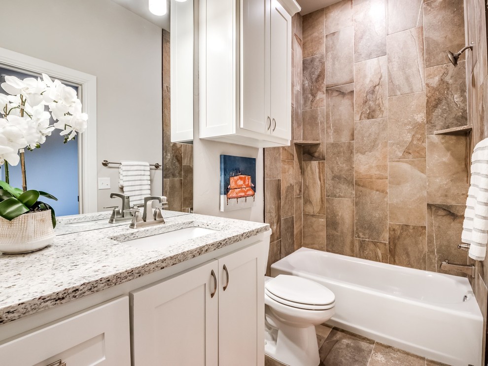 This is an example of a large country kids bathroom in Oklahoma City with shaker cabinets, white cabinets, an alcove tub, a shower/bathtub combo, a one-piece toilet, multi-coloured tile, ceramic tile, beige walls, ceramic floors, an undermount sink, granite benchtops, beige floor, a shower curtain and multi-coloured benchtops.