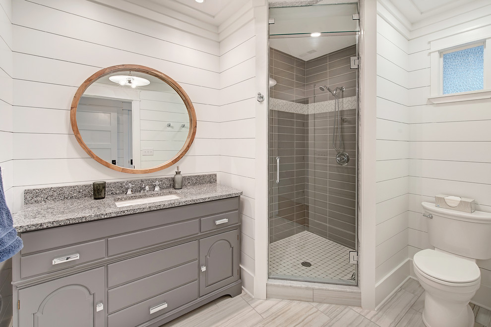 This is an example of a mid-sized country 3/4 bathroom in Baltimore with raised-panel cabinets, grey cabinets, an alcove shower, a two-piece toilet, gray tile, porcelain tile, white walls, porcelain floors, an undermount sink, granite benchtops, grey floor and a hinged shower door.