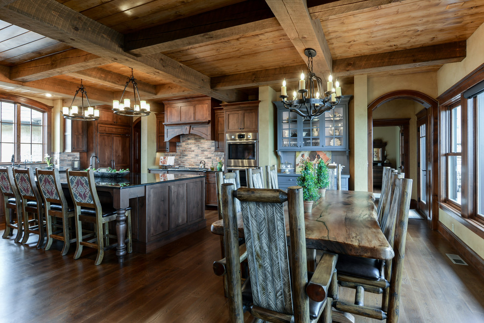 Inspiration for a mid-sized country l-shaped eat-in kitchen in Other with an undermount sink, shaker cabinets, medium wood cabinets, brick splashback, stainless steel appliances, with island and brown floor.